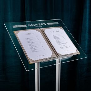 Floor-standing acrylic hostess stand with a raised lip holding a menu, showing the twin-post metal base.