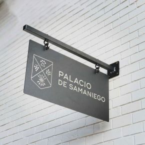 Black engraved metal hanging sign with silver logo engraving on a powder coated black wall bracket