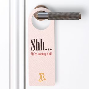 Photo of a leather door handle sign with a customised print, door is white with a brushed metal door handle.